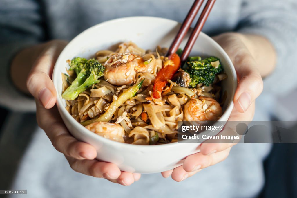 Female holding a bowl of seafood thai noodles