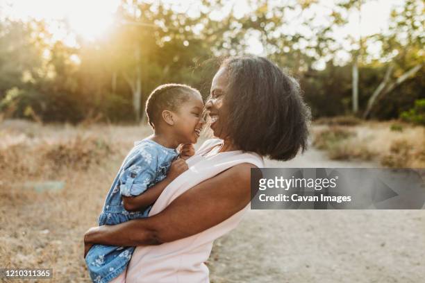 close up of happy grandmother holding young granddaughter in sun - black family reunion stock pictures, royalty-free photos & images