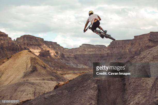 rear view of young male jumping with mountain bike in desert landscape - スタントバイク ストックフォトと画像