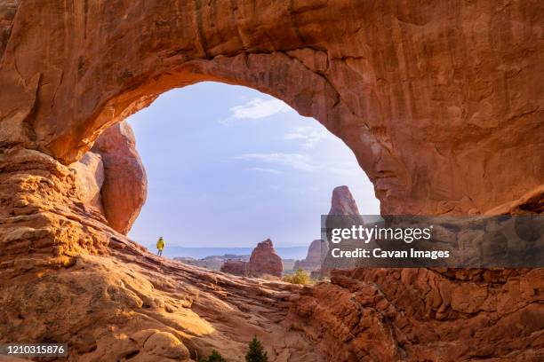 female hiker framed in the north window against blue sky in arches - moab utah fotografías e imágenes de stock