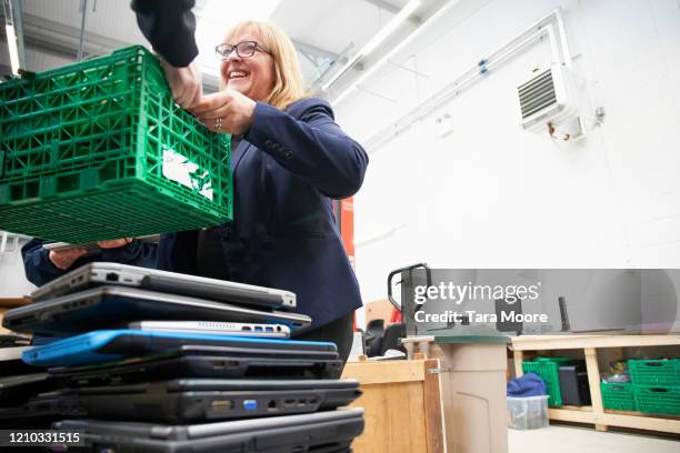 mature woman with crate of used laptops at recycling centre - femalefocuscollection stock-fotos und bilder