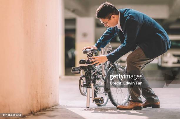 een aziatische chinese mannelijke witteboordenarbeider die klaar wordt om met zijn vouwende fiets als vervoer woon-werkverkeer te werken - folding bike stockfoto's en -beelden