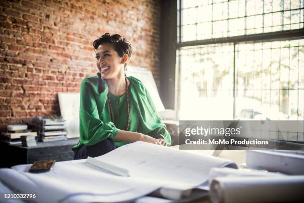 businesswoman looking over architecture blueprints in office - small business stock pictures, royalty-free photos & images