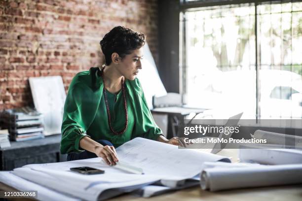 businesswoman looking over architecture blueprints in office - architekt stock-fotos und bilder