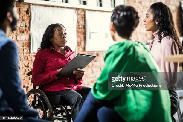 businesswoman in wheelchair leading group discussion in creative office - disabilitycollection ストックフォトと画像