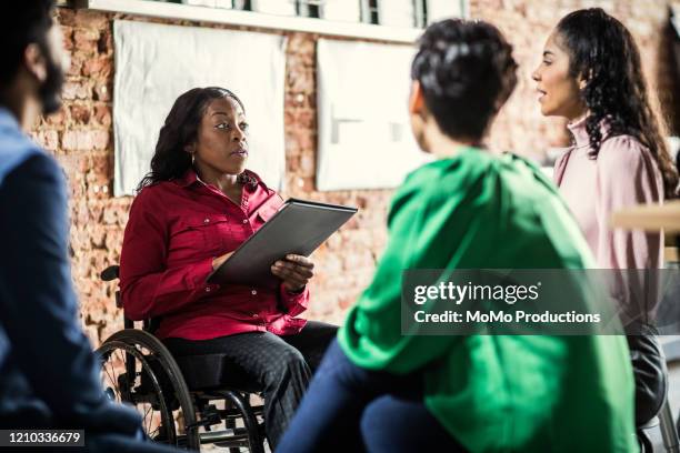 businesswoman in wheelchair leading group discussion in creative office - disabilitycollection stockfoto's en -beelden