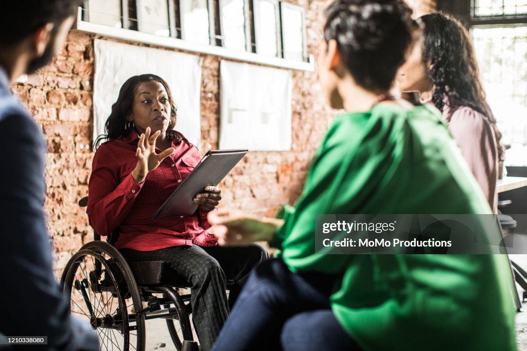 Businesswoman in wheelchair leading group discussion in creative office
