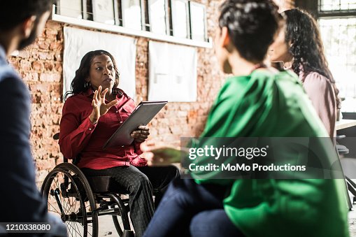Businesswoman in wheelchair leading group discussion in creative office Businesswoman in wheelchair leading group discussion in creative office
