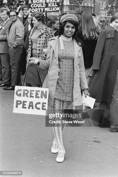Fijian protestor Sneh Sym, wearing patterned leggings and a patterned mini dress, carrying a bag on which is written 'green peace' at a CND...