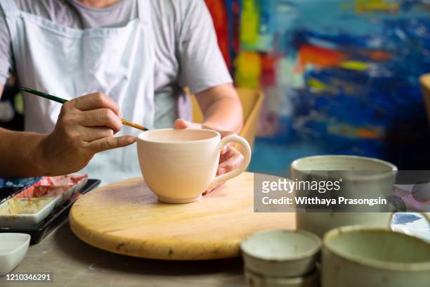 closeup shot of a man painting a cup in her small crafts workshop - painting pottery stock pictures, royalty-free photos & images