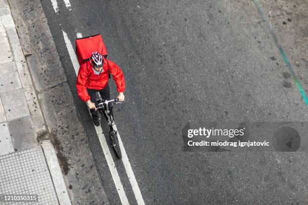 liefermann fährt fahrrad auf der stadtstraße auf dem weg zum kunden - fahrradkurier stock-fotos und bilder