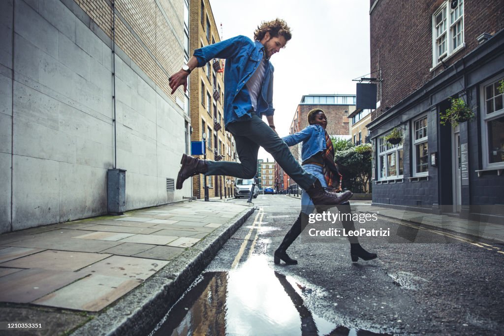 Pareja joven saltando un charco después de la tormenta