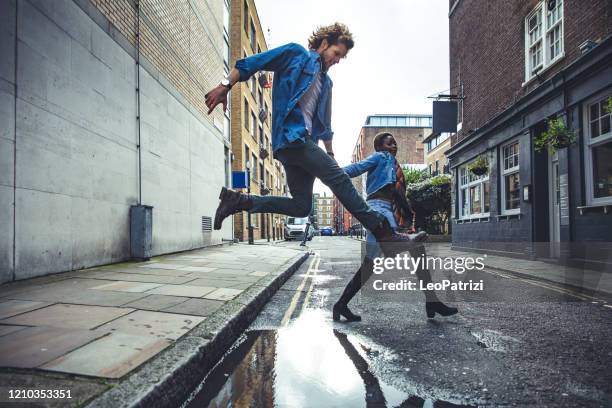 pareja joven saltando un charco después de la tormenta - puddle fotografías e imágenes de stock