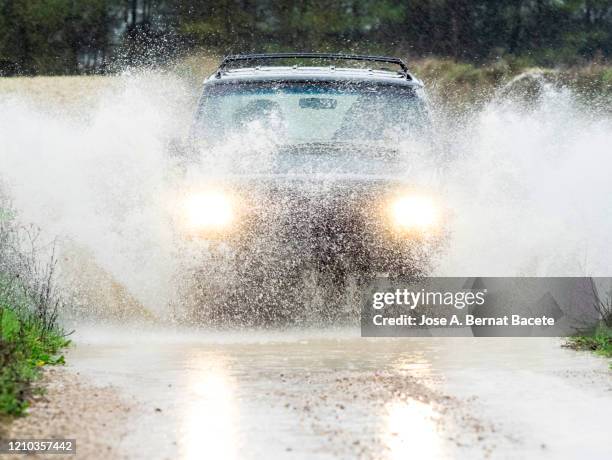 4x4 vehicle on muddy road splashing past a large puddle of rainwater, spain. - torrential rain foto e immagini stock