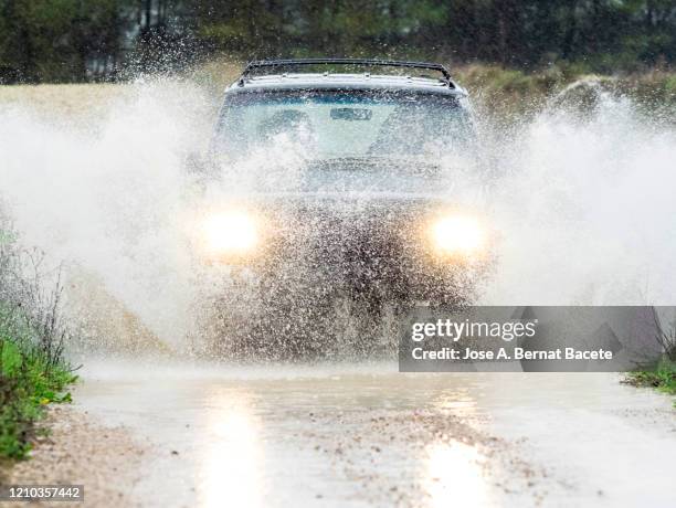 4x4 vehicle on muddy road splashing past a large puddle of rainwater, spain. - torrential rain stockfoto's en -beelden