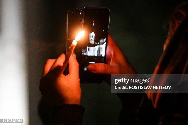 Russian Orthodox believer holds a candle and a mobile phone as she attend the Orthodox Easter service outside the church in Novosibirsk early morning...