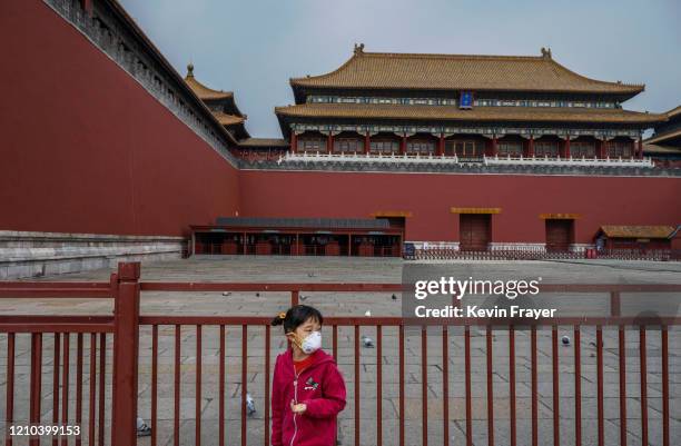 Chinese girl wears a protective mask as she feeds birds outside the gate of the Forbidden City, which remains closed to visitors, on April 19, 2020...