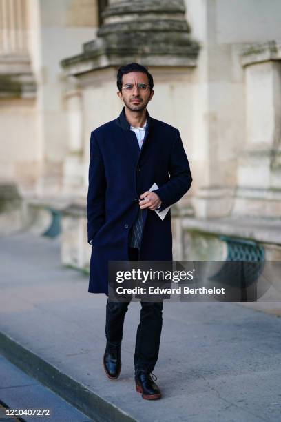 Imran Amed, founder and CEO of Business of Fashion, wears glasses, a navy blue long coat, blue denim pants, black leather shoes, outside Vuitton,...