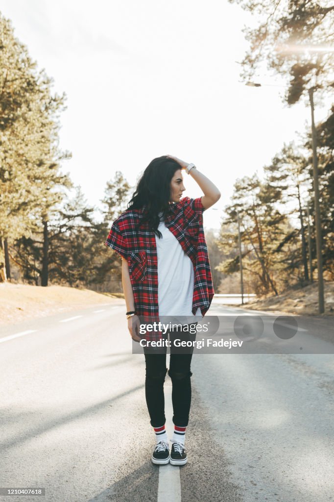 Awesome girl in trendy clothes standing on the road at the forest. Beautiful look, spring. Soft colours.