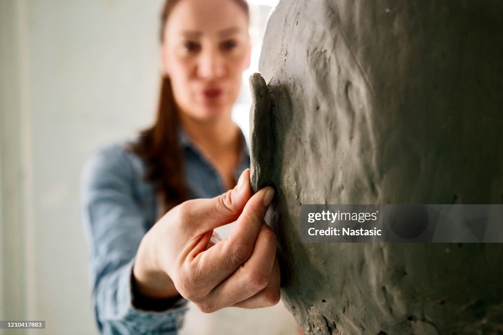 Joven trabajando en una escultura de cabeza de arcilla en taller trabajando en una oreja