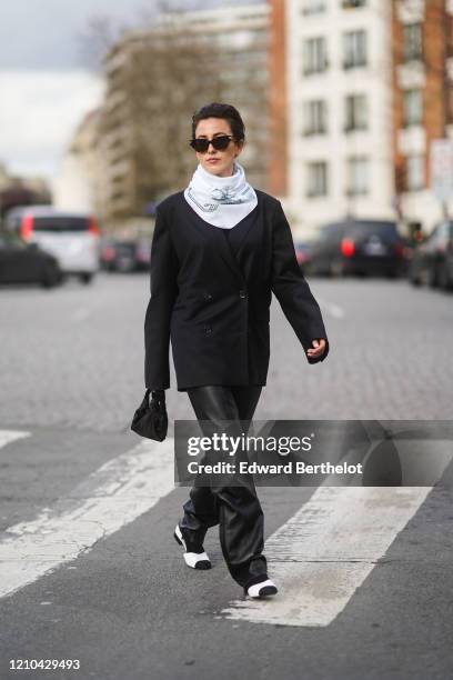 Sylvia Haghjoo wears sunglasses, a white scarf, an oversized blazer jacket, black leather pants, shoes, a mini bag, outside Lacoste, during Paris...