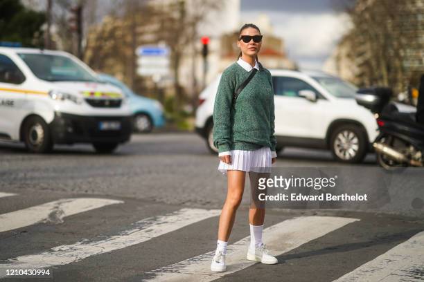 Sophia Roe wears sunglasses, a white polo shirt, a green pullover from Lacoste, a white pleated mini skirt, white socks, sneakers, outside Lacoste,...