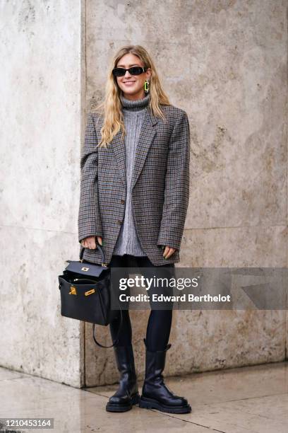 Emili Sindlev wears sunglasses, earrings, a grey turtleneck, a grey houndstooth oversized jacket, black leggings, black mid-calf boots, a black bag,...