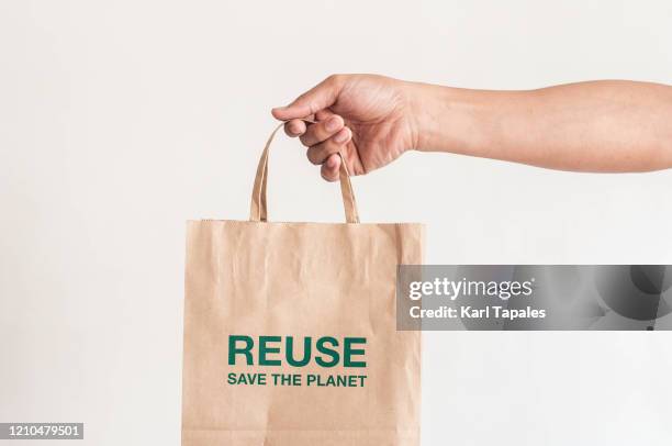 a close-up view of a young person holding a paper bag with phrase saying: "reuse, save the planet" on a white background - holding paper fotografías e imágenes de stock