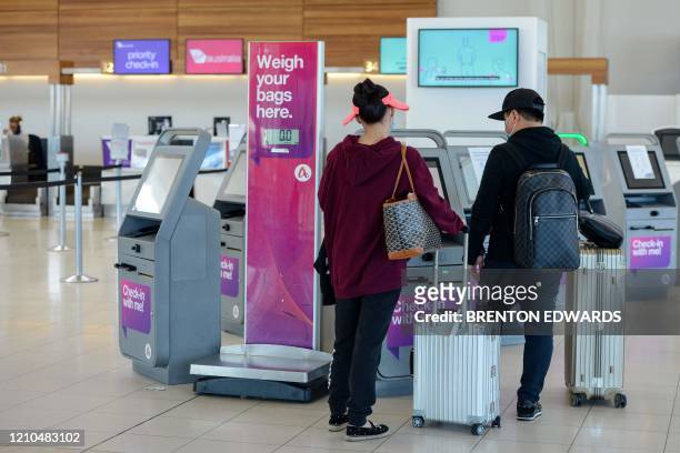 Two travellers look at self-check-in machines at Virgin Australia in the departures area at Adelaide Airport in Adelaide on April 21, 2020. -...