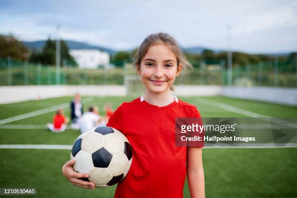 a small girl with soccer ball standing outdoors on football pitch, looking at camera. - football pitch bildbanksfoton och bilder