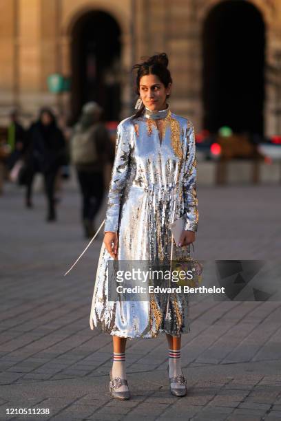 Guest wears a silver shiny glitter turtleneck dress, an A-shaped earring, a yellow and purple bejeweled bag, striped socks, bejeweled shoes, outside...