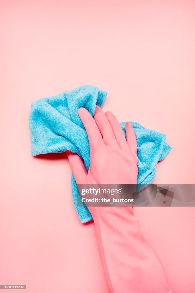 Hand in pink glove with blue cleaning rag on pink background, house cleaning