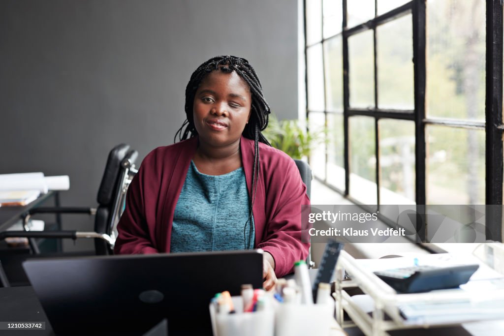 Portrait of smiling young businesswoman with a visual impairment using laptop at modern workplace