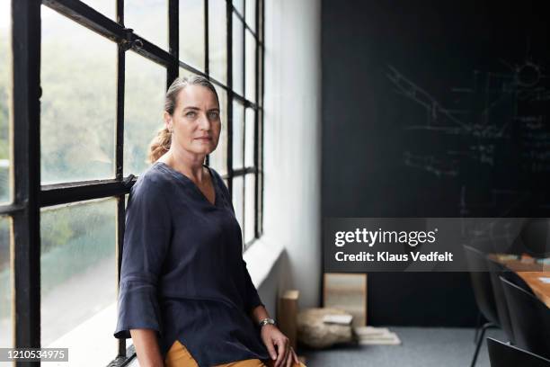 entrepreneur by window in board room at workplace - serious women stock pictures, royalty-free photos & images