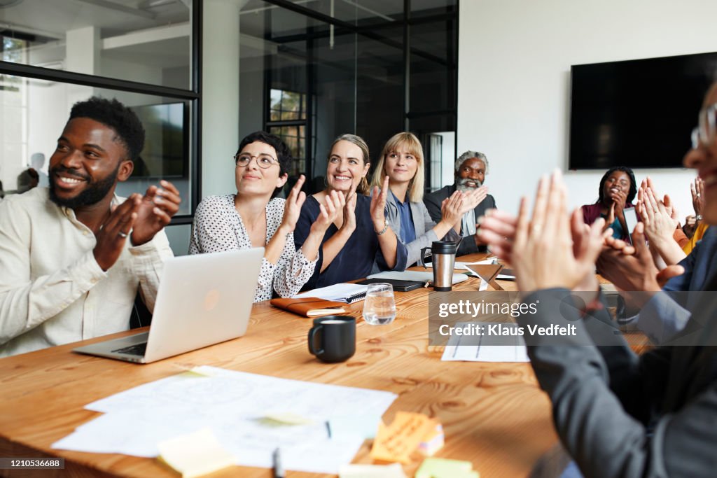 Executives clapping by table in office meeting