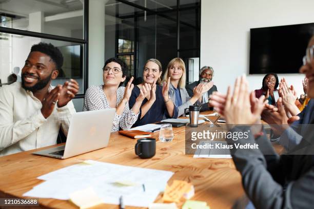 executives clapping by table in office meeting - vencer imagens e fotografias de stock