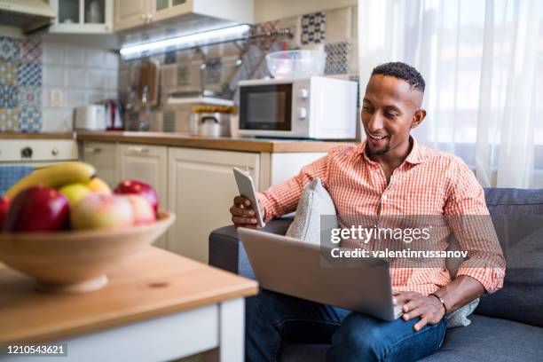 ラップトップで働き、自宅でスマートフォンを使用しているアフロラテン系の男性 - business man sitting banking ストックフォトと画像