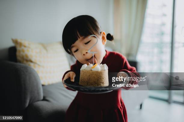 portrait of a cute little girl holding a birthday cake celebrating her two years old birthday and sticks out her tongue attempting to lick the cake - 2 3 years stock-fotos und bilder
