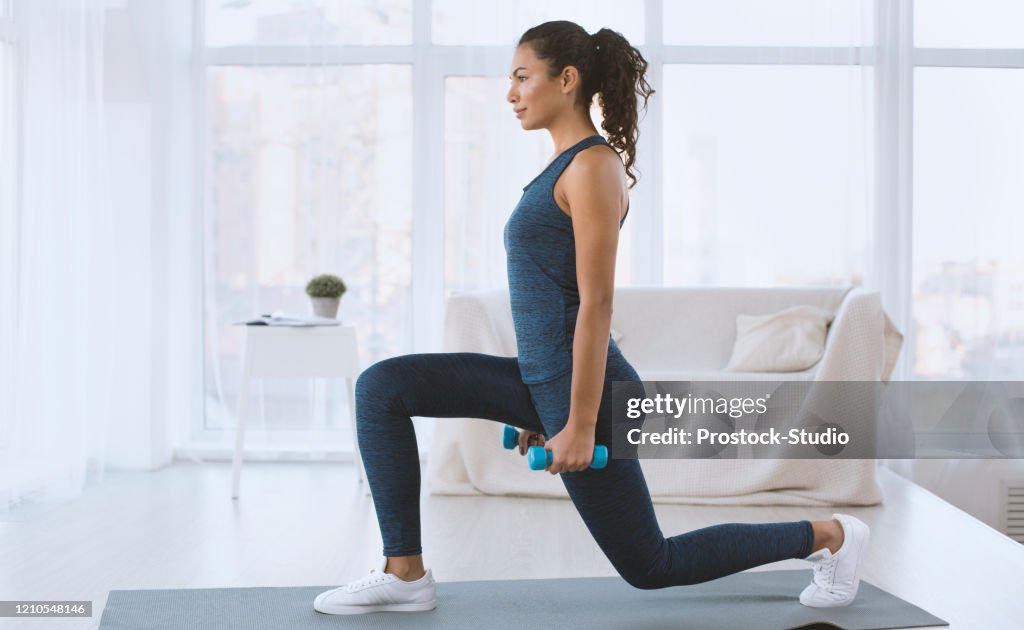 Slim Hispanic girl doing lunges with dumbbells at home, empty space