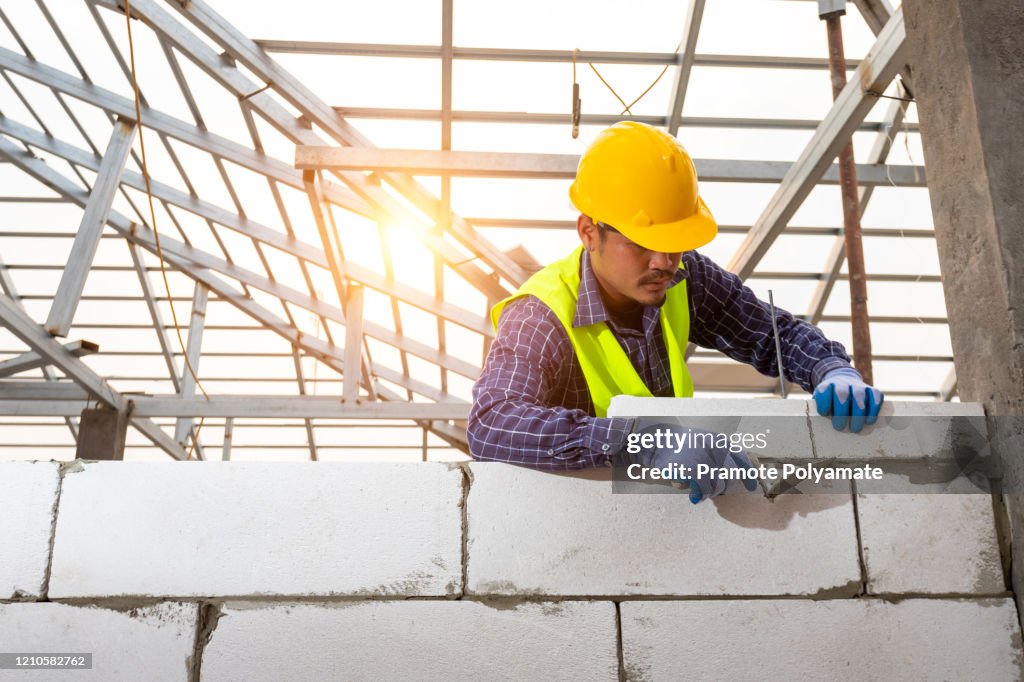 Bricklayer builder working with autoclaved aerated concrete blocks. Walling, installing bricks on construction site, Engineering and constructions concepts.