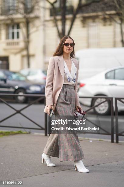 Erika Boldrin wears sunglasses, a pale pink blazer jacket, a white low neck shirt, checked large flared pants, white boots, outside Miu Miu, during...