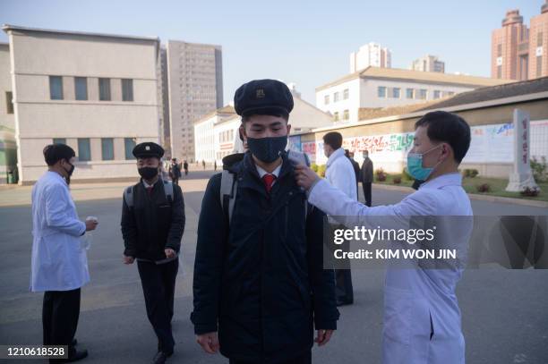 Students wearing face masks disinfect their hands and undergo a temperature check as they arrive for a lecture on preventative measures against the...