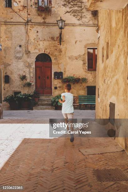 rear view young boy running away in pienza street, toscana,italy - village boy foto e immagini stock