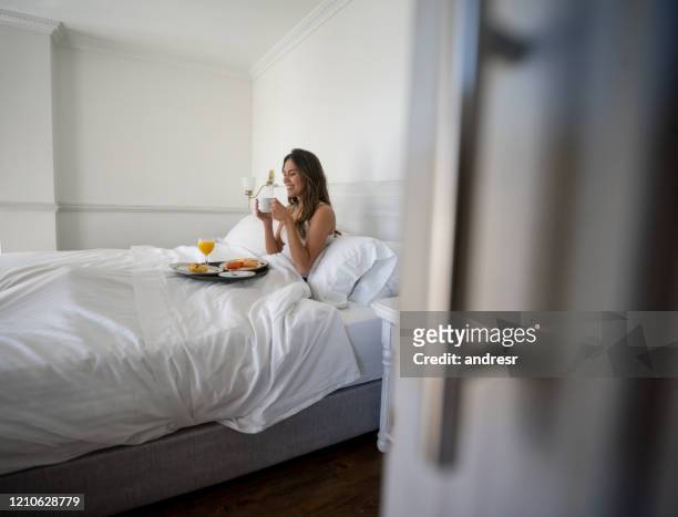 gelukkige vrouw die ontbijt op bed bij haar hotelruimte eet - ontbijt op bed stockfoto's en -beelden
