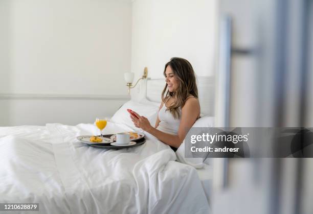 donna in un hotel che sms mentre fa colazione a letto - colazione hotel foto e immagini stock