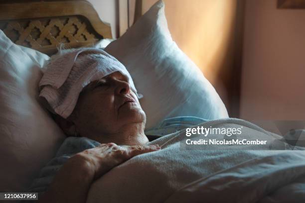 zieke uitgeputte hogere vrouw in bed met nat washandje op haar voorhoofd - indecisive stockfoto's en -beelden