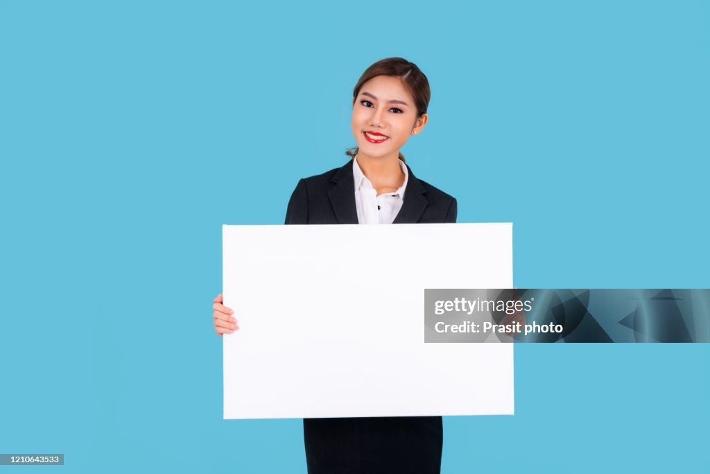 Banner of young happy Asian businesswoman in suit feeling happiness and holding Empty white canvas frame for text or business advertising isolated on cyan background