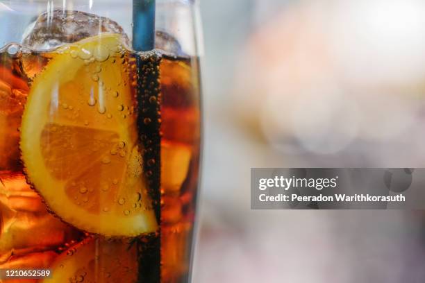 close up or macro view at sliced piece of lemon inside glass of cold drink with cola soda and ice cube and background of abstract bokeh. - restaurant düsseldorf stock-fotos und bilder