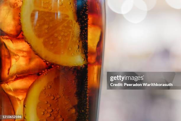 close up or macro view at sliced piece of lemon inside glass of cold drink with cola soda and ice cube and background of abstract bokeh. - restaurant düsseldorf bildbanksfoton och bilder