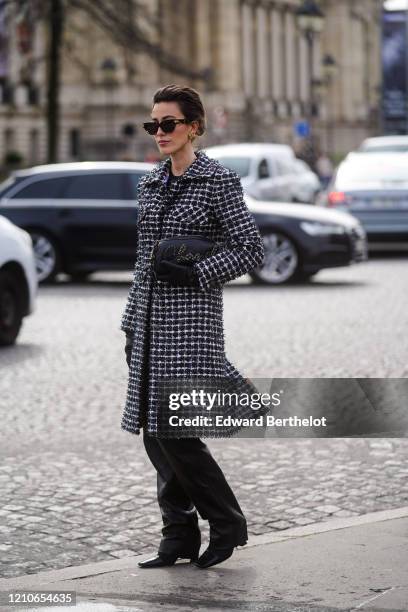 Julia Haghjoo wears sunglasses, a Chanel bag, leather gloves, a black and white tweed long coat, black leather pants, pointy shoes, outside Chanel,...